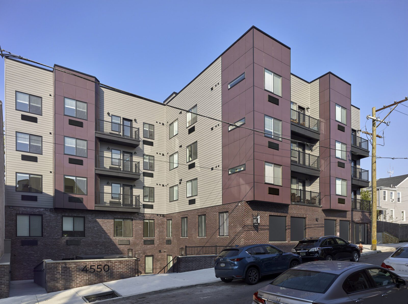 exterior photo of the Aster, the building's facade is maroon & gray fiber cement panels above a wine-colored brick base
