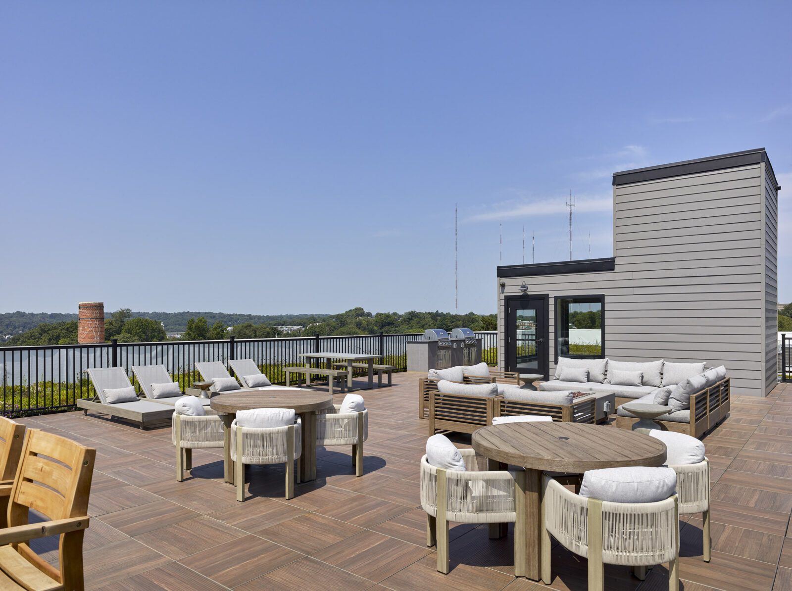 photo of The Aster's roof deck, showcasing a number of round tables, couches surrounding a fire pit, lounge chairs, and grills