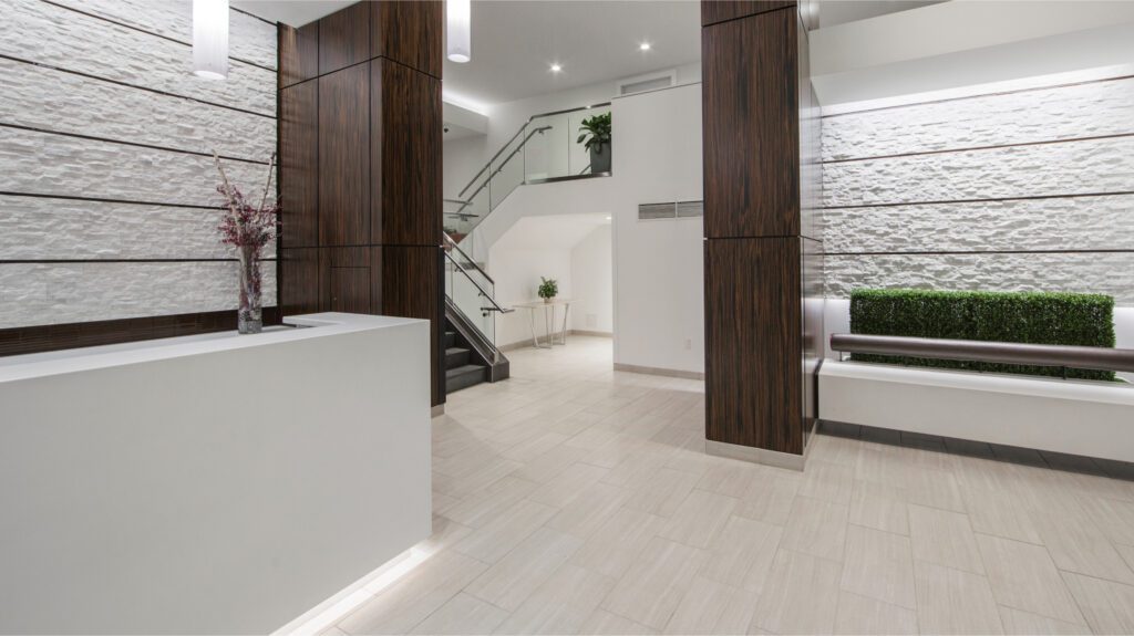 A lobby with a front desk, a plant bed, and stairs behind the pillar