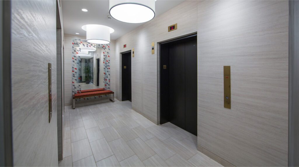 Elevators located in the corridor, with a large mirror and a bench situated in front of them.