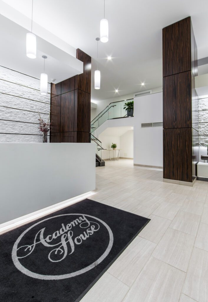 A lobby with the front desk and a rug with 'Academy House' written on it