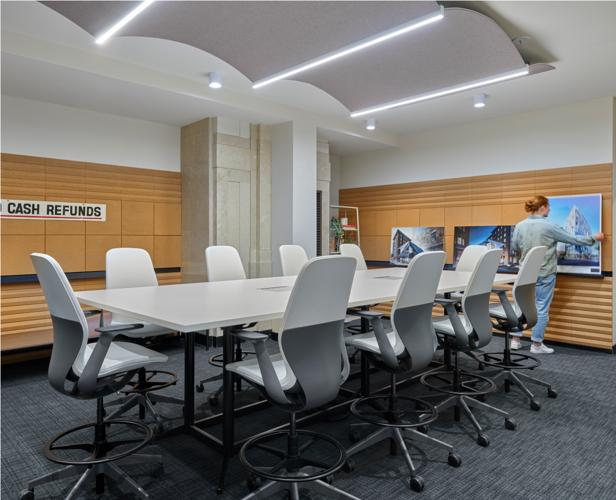 Conference room with a big desk and a lot of chairs. A man is placing some photos on the wall